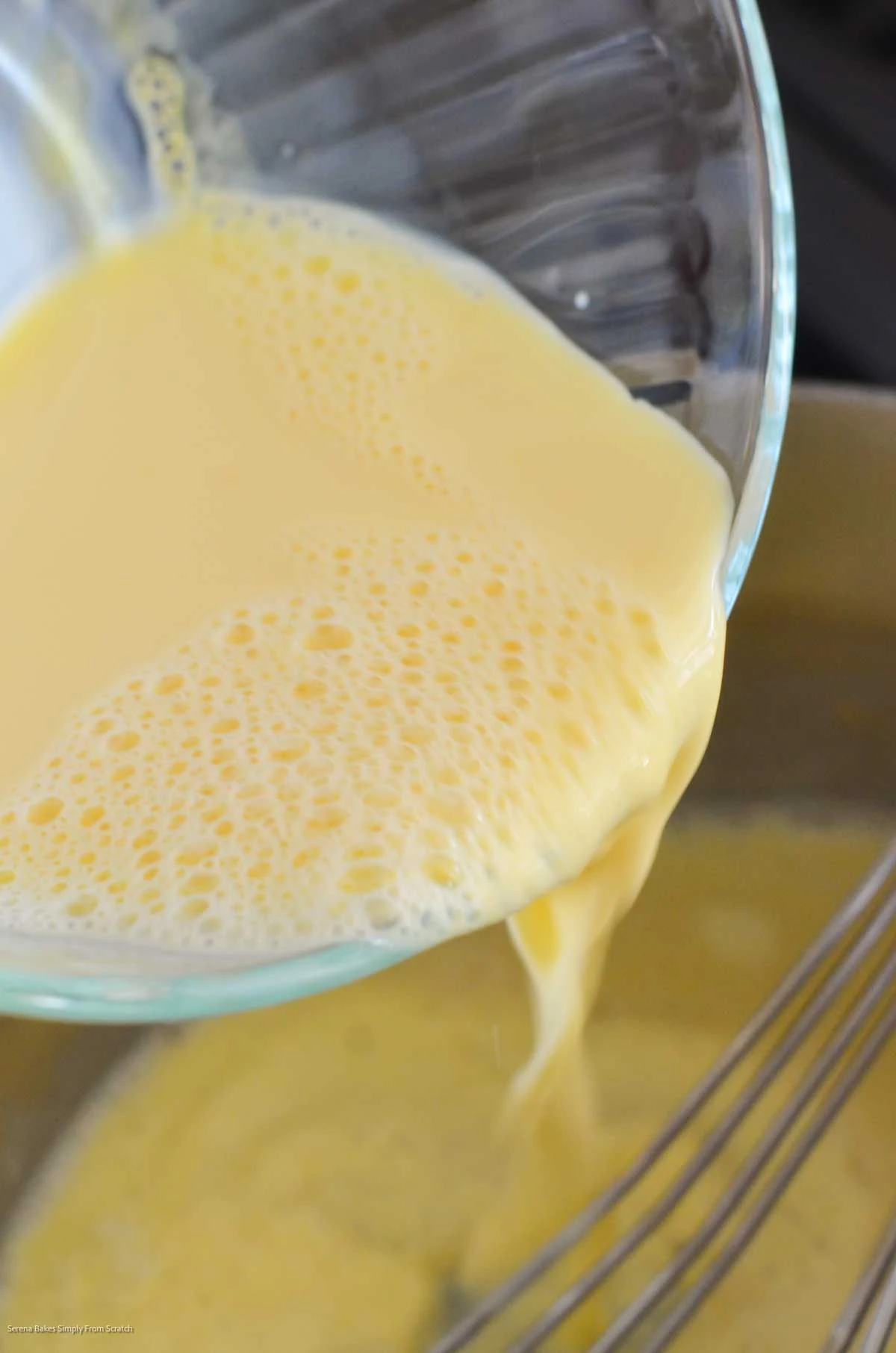 Whisking egg yolk and milk mixture into flour mixture in a stainless steel pan.