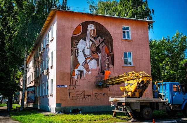 Художник рисует на фасаде дома в люльке крана
