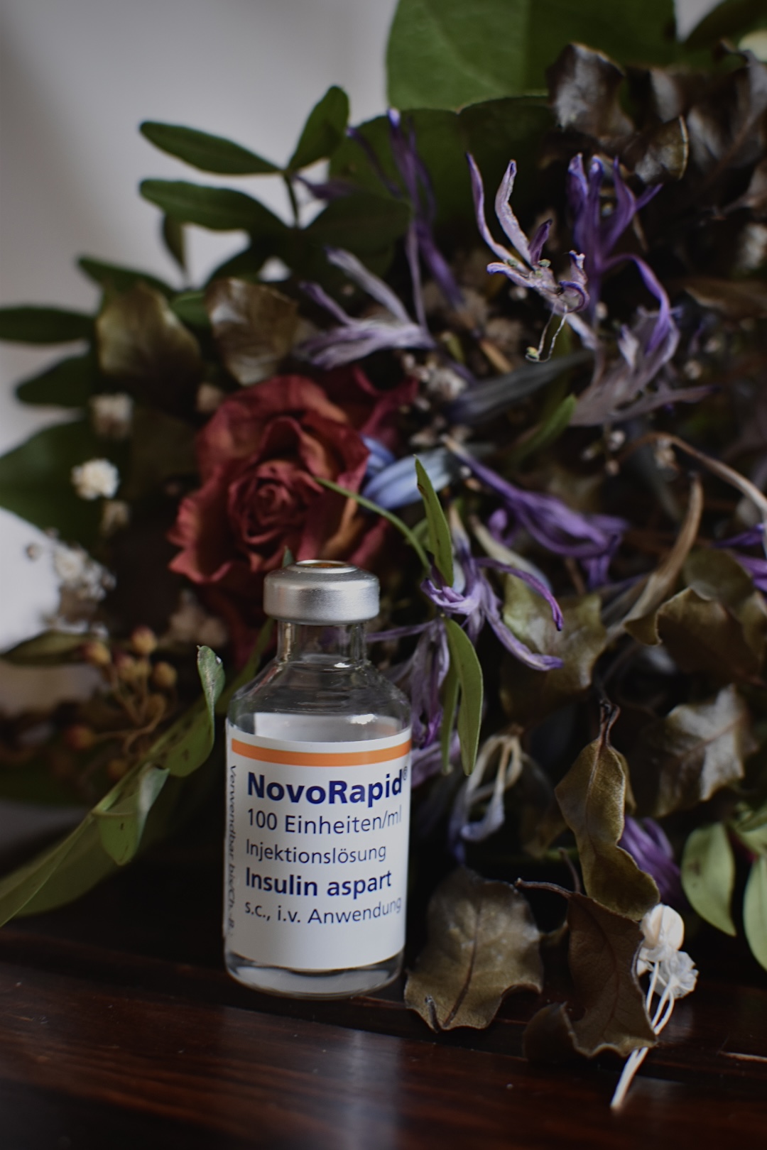 Eine Insulinflasche steht vor einem bunten Trockenblumenstrauß.