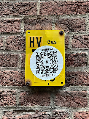 Aanwijsplaat in Den Haag, grotendeels bedekt met een sticker met een QR-code en daarboven en -onder de tekst 'Ethereal'