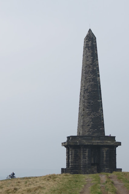 A close-up of the tower against open sky. To the left, a motorcyclist is silhouetted on his bike.