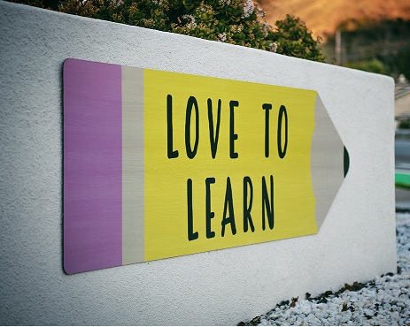 A sign that reads 'love to learn' on a large pencil shape on a concrete wall