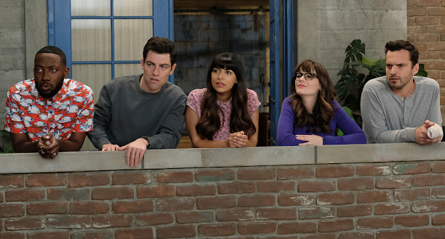 The cast of New Girl. They are stood on a balcony, looking off at something the distance.