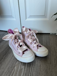 A pair of pastel pink high top converse shoes with large ribbon laces and large grommets to accommodate.