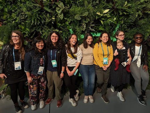 A group of Android Developers and a baby, standing against a headge of lush greenery, smiling