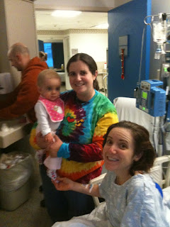 My sister Sam holding Riley by my hospital bed.  I'm sitting up smiling.