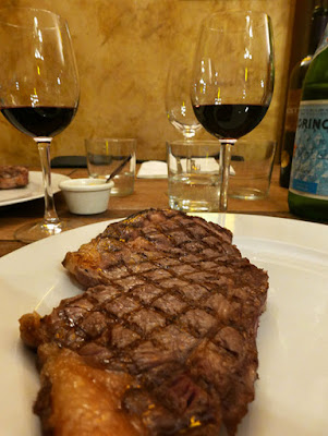 A steak with visible criss-cross char lines and two glasses of wine behind it.