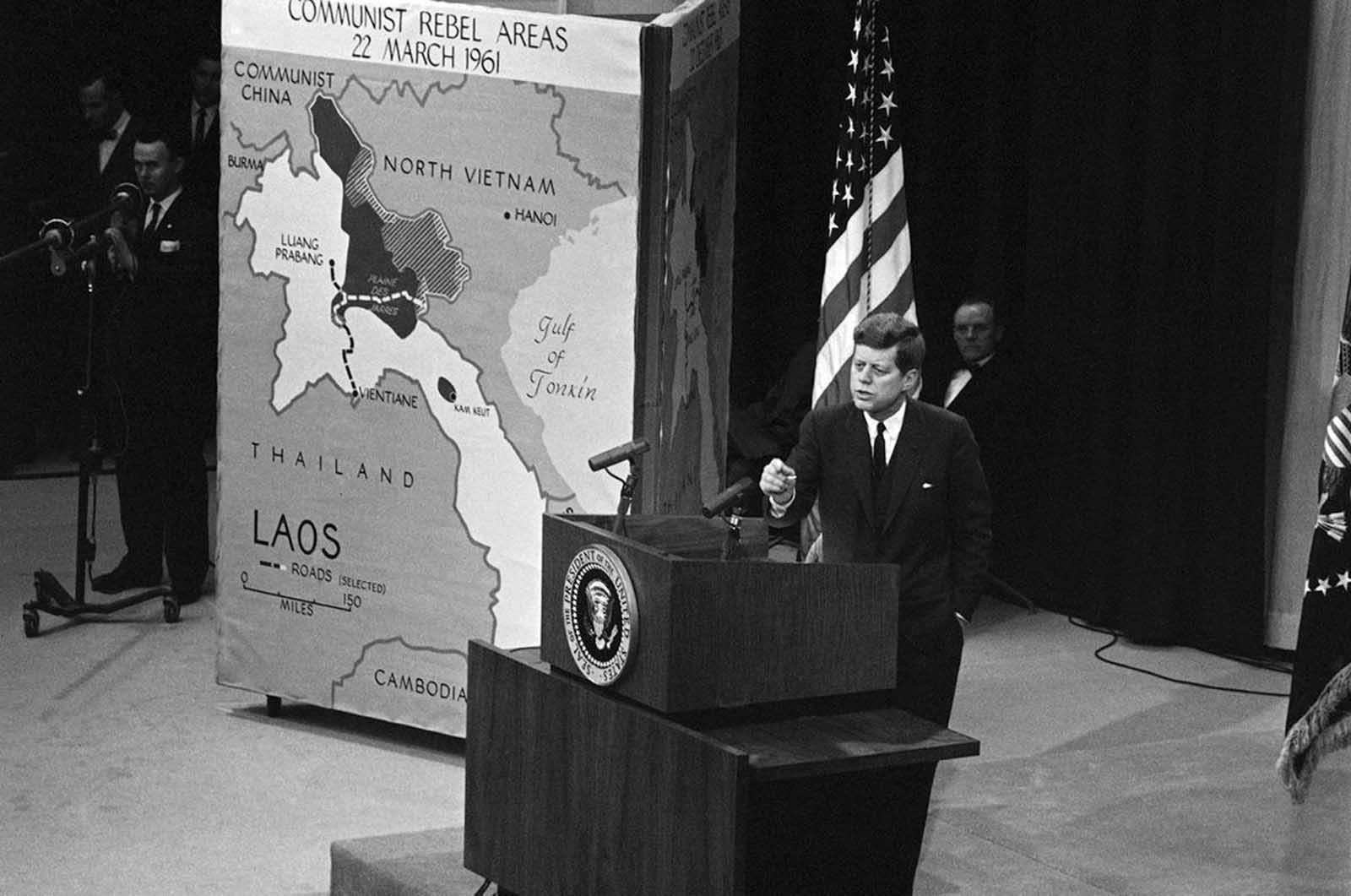 President Kennedy speaks to reporters at a nationally televised news conference in the State Department auditorium, on March 23, 1961. The Chief Executive at the opening of the conference discussed the Laos situation and used three different maps, picturing how pro-communist rebels have gained ground in the last seven months in Laos. The map at left was used by Kennedy to Show communist rebel areas as of March 22 which, he said, are indicated by the dark and shaded portions