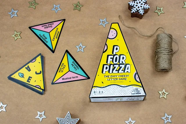 A wedge shaped cardboard box for the P for Pizza game, next to some triangular shaped pieces. On one side they have 3 letters and on the other 3 categories