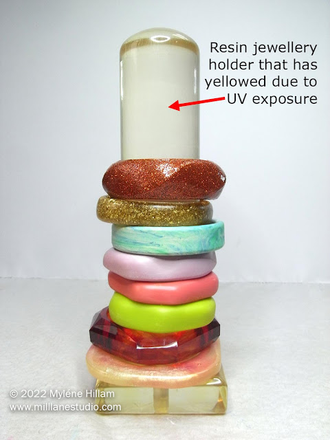 Clear resin bangle pillar stand that has yellowed due to UV exposure. The pillar is stacked with colourful resin bangles.