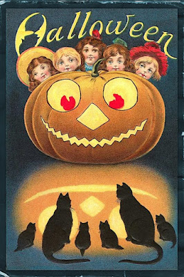 A vintage Halloween greeting card with five girls looking from over the top of a jack-o-lantern and six cats sitting in front of it.