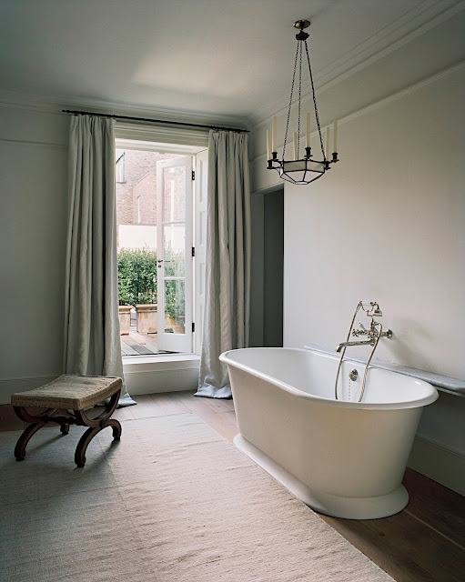 modern white bathtub with chandelier above and view to the garden