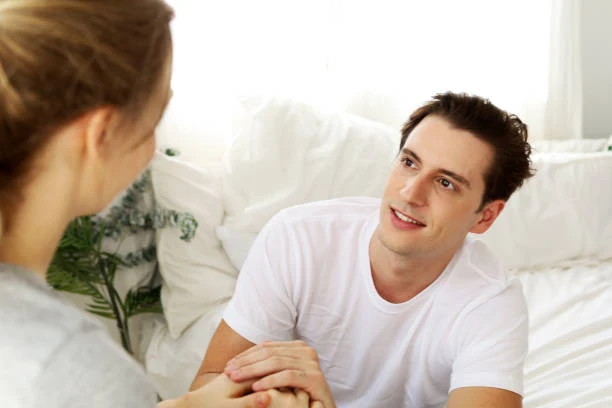 Wife holding husband's hand while he rests in bed, symbolizing support and recovery.