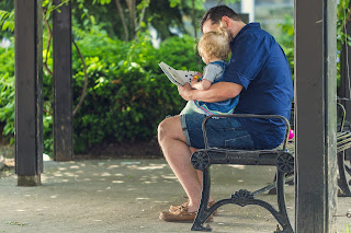 an adult and toddler look at a board book together, facing away from the camera