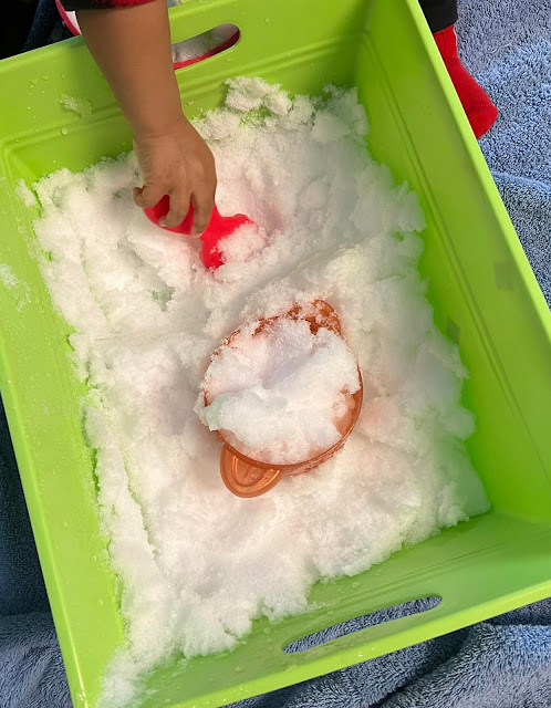 a child's hand playing with snow in a green plastic tub.