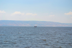 lago de tiberiades vendo-se um barco navegando ao longe e por trás as montanhas da Síria
