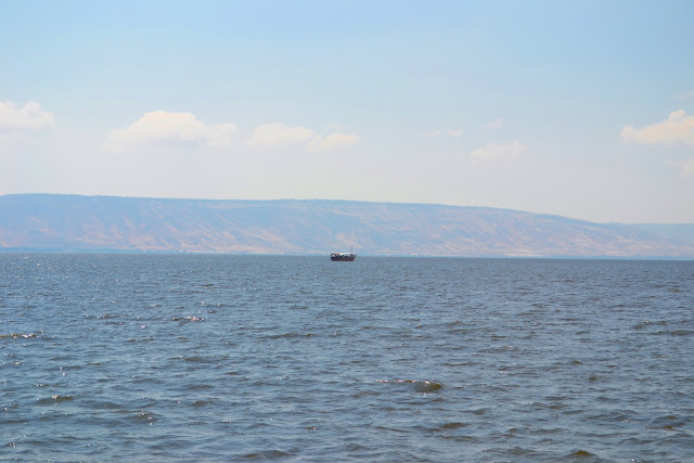 lago de tiberiades vendo-se um barco navegando ao longe e por trás as montanhas da Síria