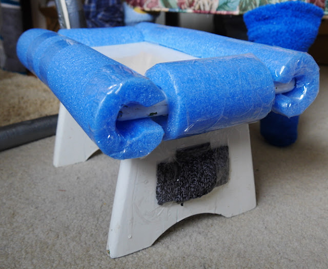 A white foot stool with blue foam taped around its edges.