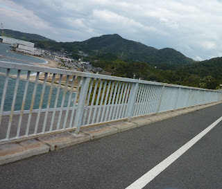 View over the side of the Hakata Oshima bridge with mountains of Oshima and a beach visible. On the Shimanami Kaido Bikeway