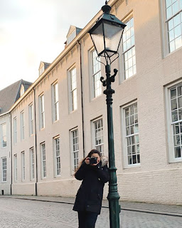 Fotografe Texas van Egmond leunt tegen een oude lantaarnpaal in Breda, terwijl ze een foto maakt.
