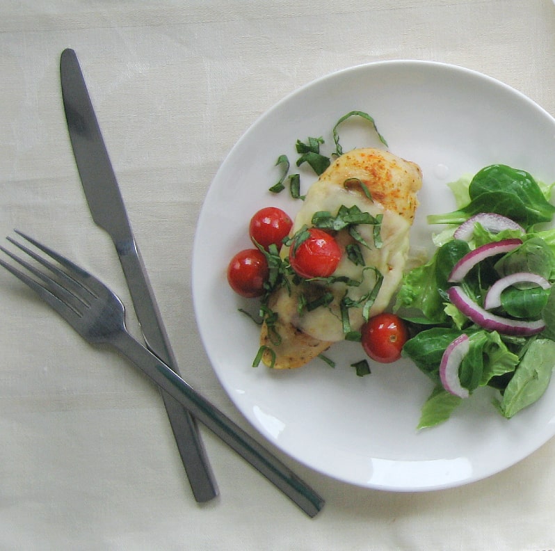 plate serving a caprese chicken breast with salad on the side