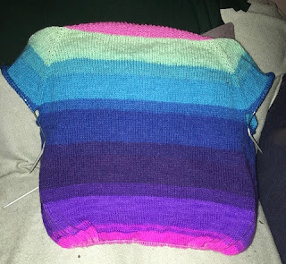 Back view of brightly coloured striped sweater. The sleeve caps are on hold, as are the bottom body stitches. The stripes are a gradient of pink, mint, teal, blue, and purple shades.