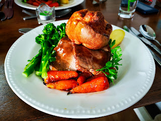 a roast dinner with meat, carrots, broccoli, and yorkshire puddings