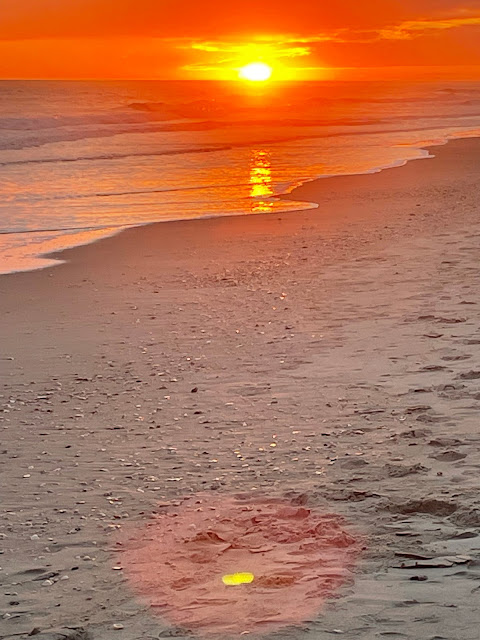 Sunset - a halo of yellow is surrounding the sun as it sets on the horizon. The sun is reflected in full form across most of the wet beachy sand in a tunnel like vision.