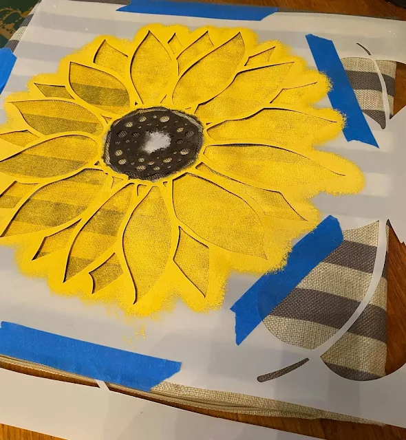 Photo of a sunflower being stenciled on a pillow cover.