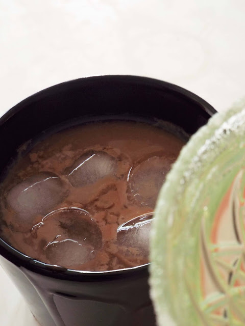 Close up of Six Feet Under. Iced chocolate rum, with ice cubes and a chocolate dripped rim, in black mug.