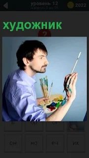 Мужчина на холсте используя кисточки в руках пишет картину с необычным выражением лица