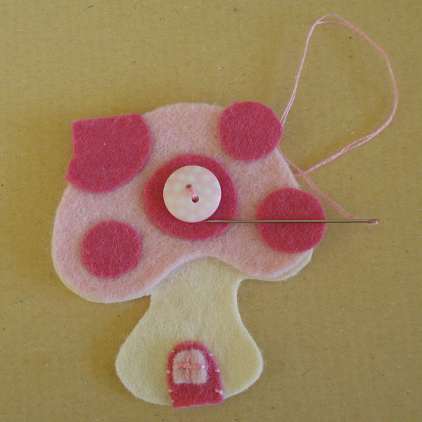 Pink button being sewn onto the pink felt mushroom shape