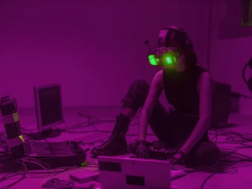 una persona con casco y gafas sentada en el suelo con computadoras portátiles y cables