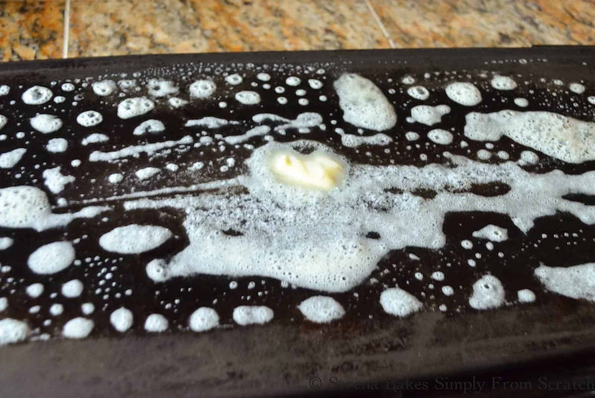 A black electric griddle with melted butter smeared all over it!