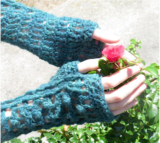 A person wearing a pair of fingerless crochet mittens. They have their hands around a small flower.