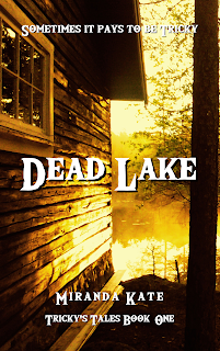 Book cover for Dead Lake, by Miranda Kate, Tricky's Tales Book one, with the tagline Sometimes it pays to be Tricky. The image depicts the side of a wood cabin on the left, with a window and roof overhang, and a tree trunk with foliage on the right, looking out between them at a mist-covered lake. The entire image is filtered with a golden yellow.