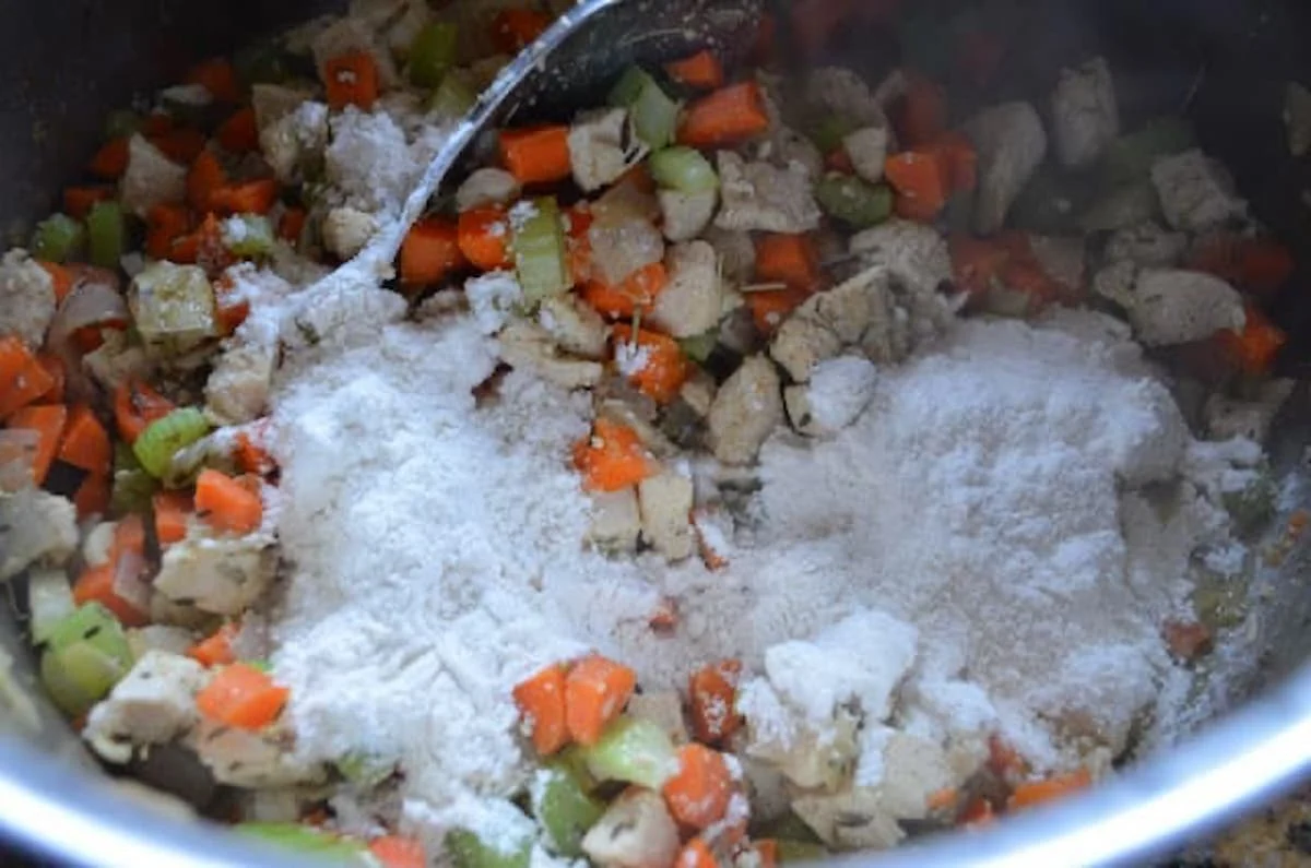 Flour added to chicken and vegetables to make roux for Chicken Pot Pie in a stainless steel pan.