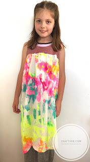 A young girl standing wearing a dress with a burgandy bodice and colourful tie-dye skirt.