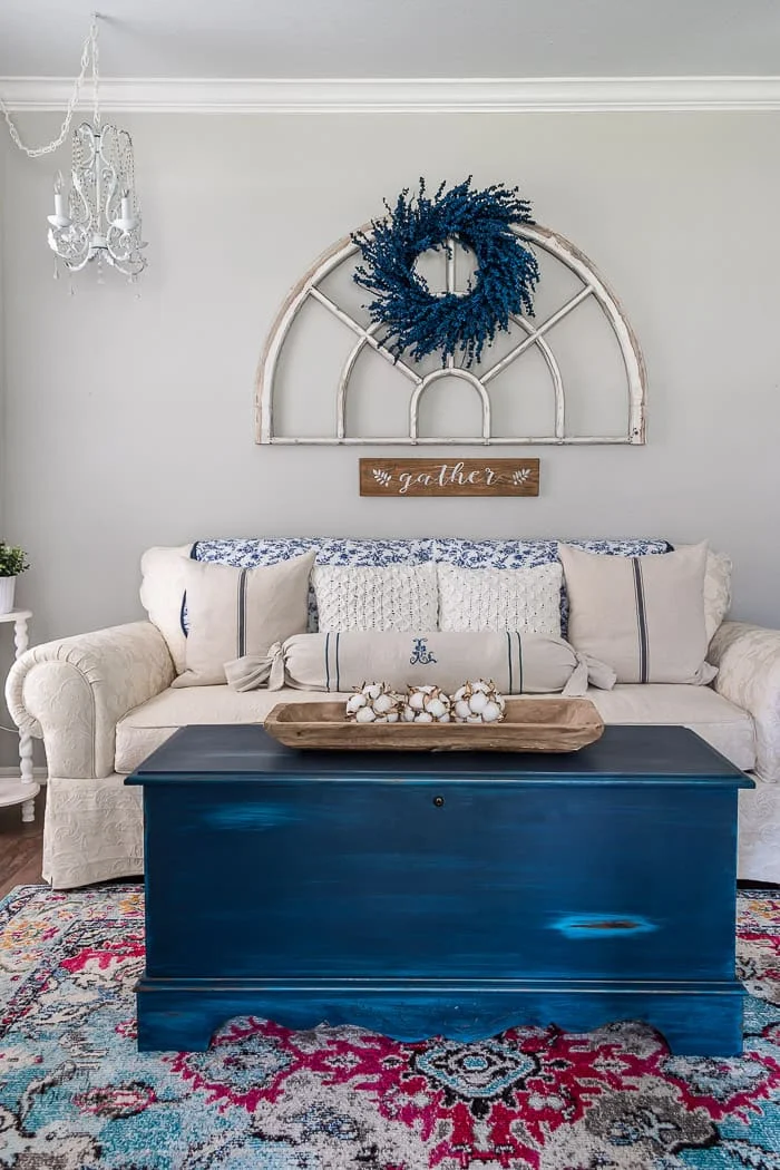 blue and white living room with grain sack pillows, blue painted trunk, antique arch window and blue berry wreath