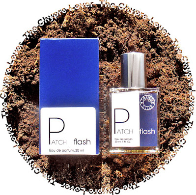 The bottle and blue cardboard box of Patch flash by Tauer (eau de parfum) lying flat on a bed of semi-dry soil