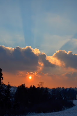 Winterlandschaft mit Sonne und großen, dunklen Wolken.