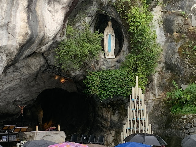 foto da Gruta de Massabiele atualmente, com um altar onde são celebradas as missas mais no fundo, a imagem de Nossa Senhora em um buraco na rocha, e um castelo de velas oferecidas pelos fiéis