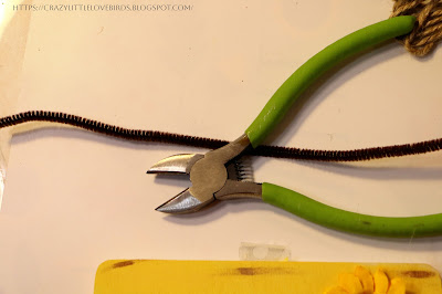 Floral cutters and pipe cleaner near yellow painted frame