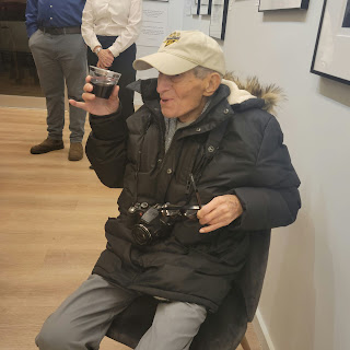 Photographer Tony Vaccaro raises a glass of red wine in a roast while seated at his Centennial Exhibition pop up in NYC, December, 2022