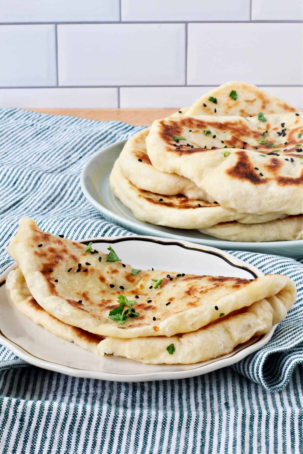 Garlic and Cheese Naan folded in half on a plate with more in the background.