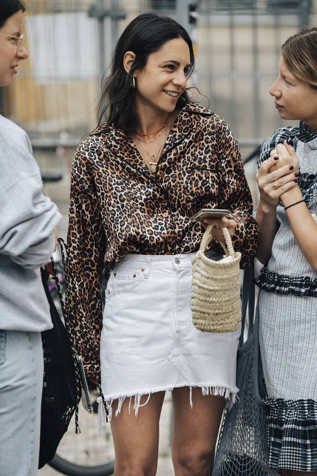 How to wear white denim skirt for summer outfit idea with leopard print shirt, layered necklaces and straw basket tote bag