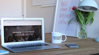 Home business work station with a computer, notepad, mobile phone, a white mug, table lamp and flowers.