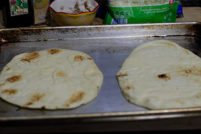 Two pieces of naan bread on a baking sheet.