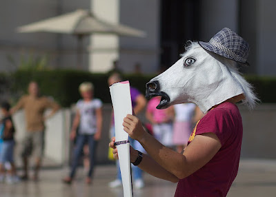 A person wearing a white horse mask and a hat, looking at a map.