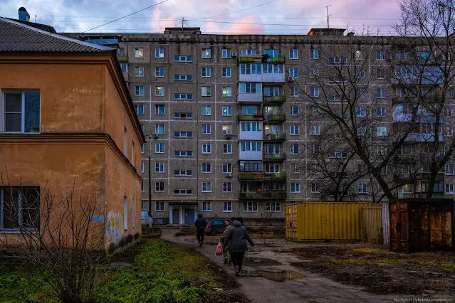 Люди идут по пешеходной дорожке к многожтажке